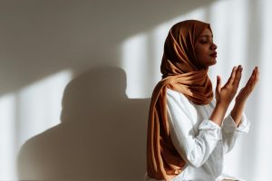 woman in a brown hijab praying with her eyes closed